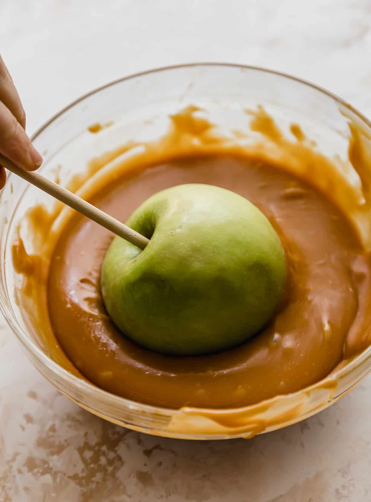 A green Granny Smith apple being dunked in caramel.