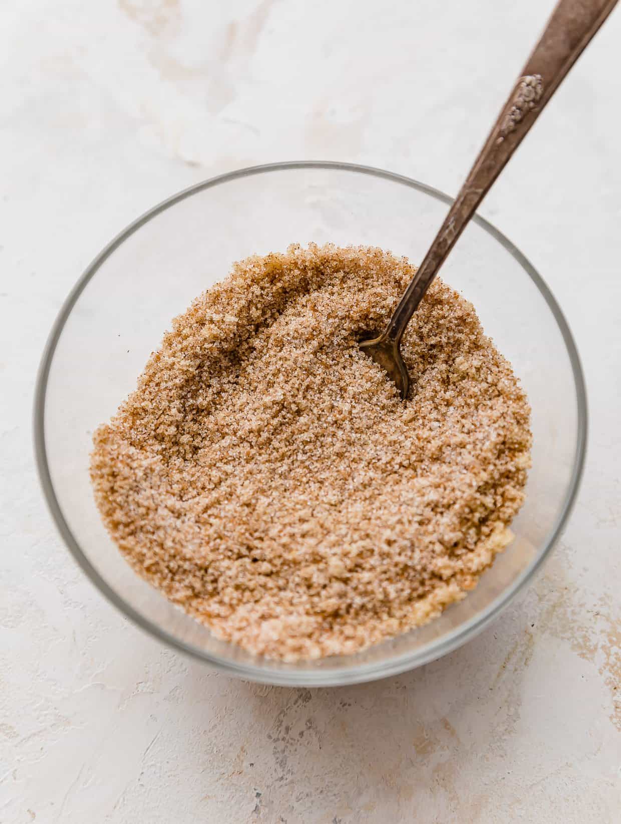 A cinnamon sugar mixture in a glass bowl on a white background.