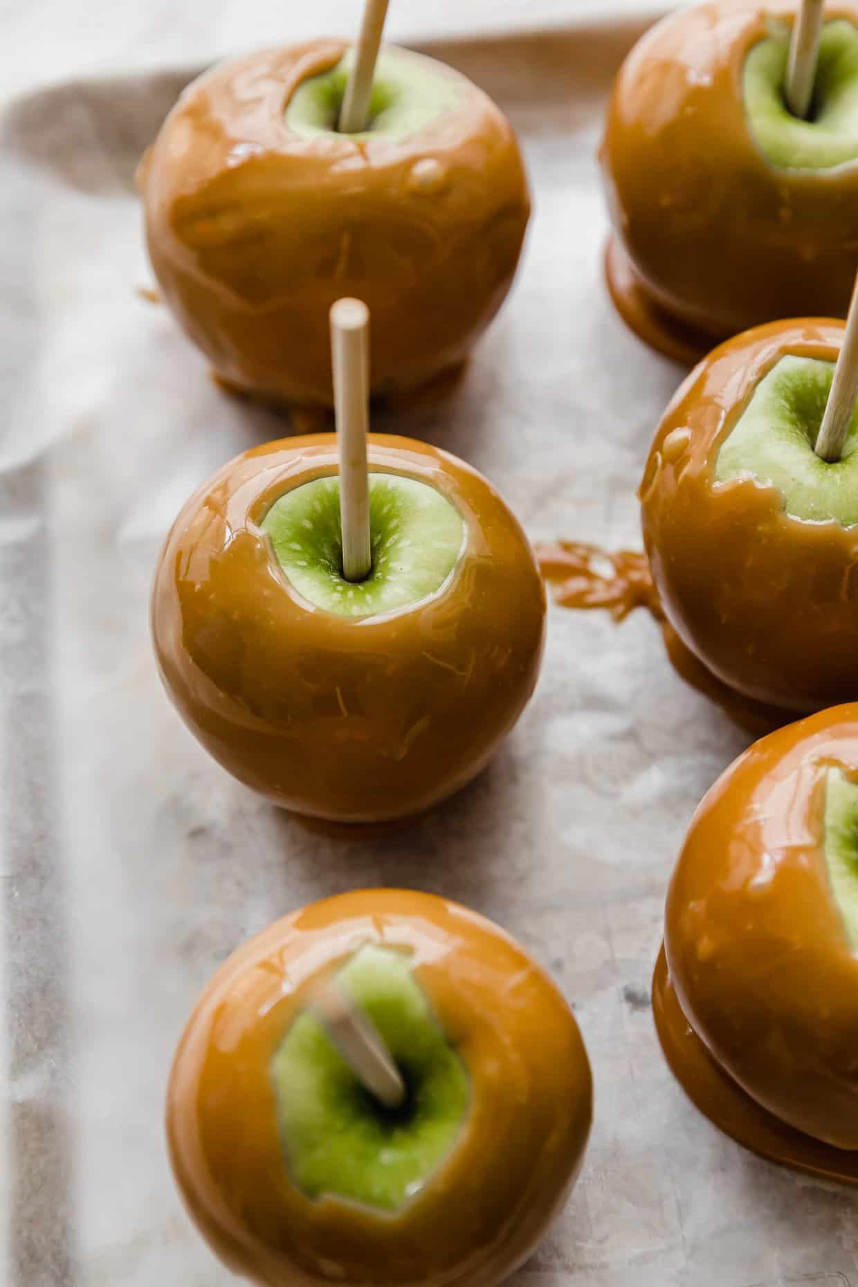 Green Granny Smith apples covered in caramel on a wax paper lined tray.