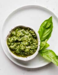 Basil pesto in a small white bowl against a white background.