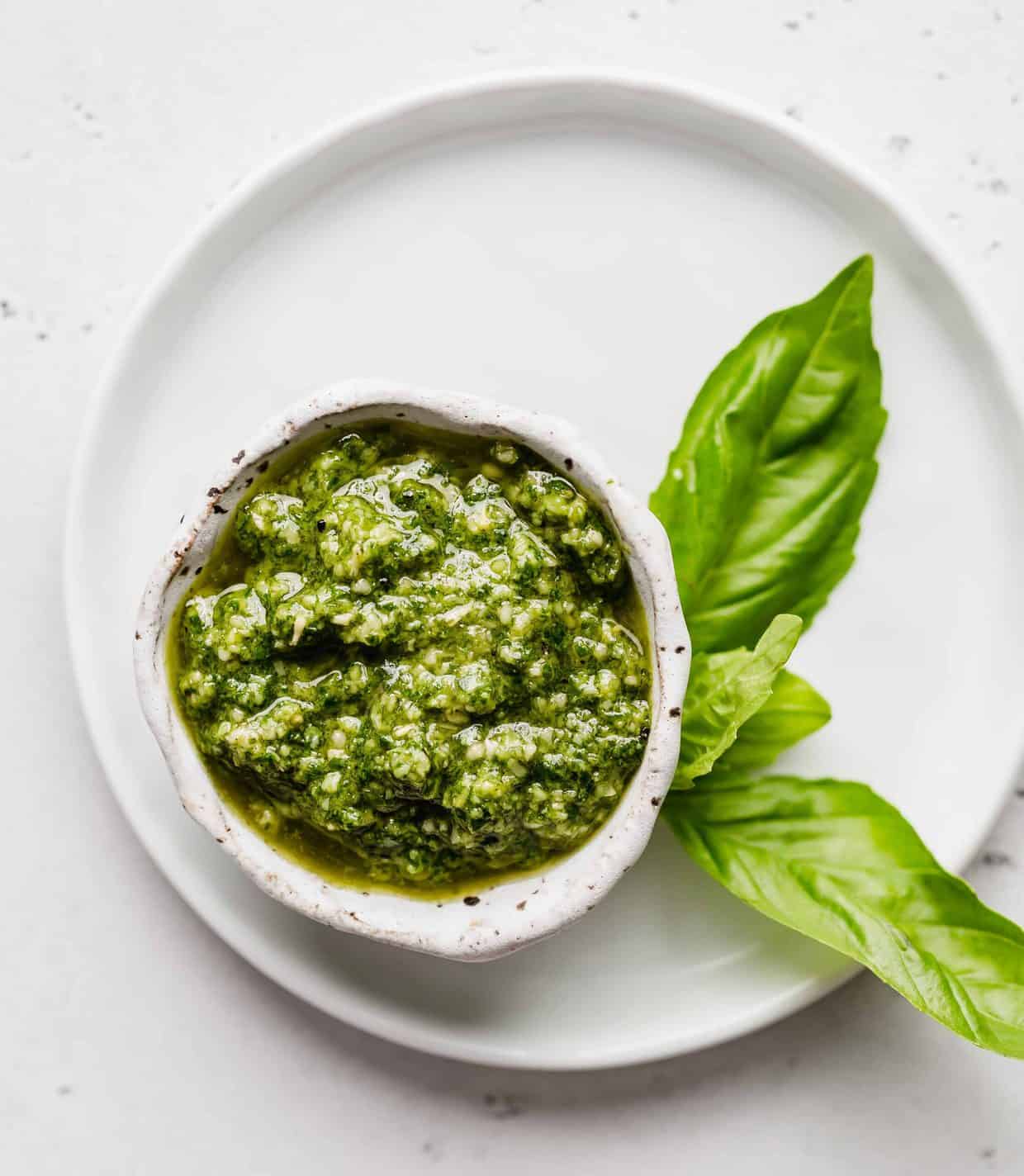 Basil pesto in a small white bowl against a white background.