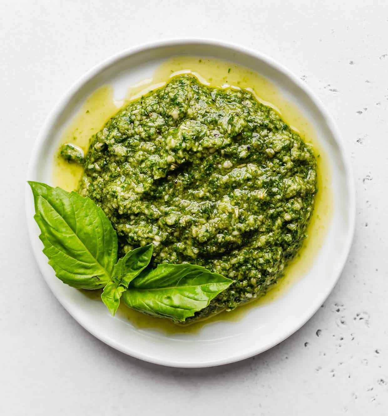 A white plate with fresh basil pesto on it.