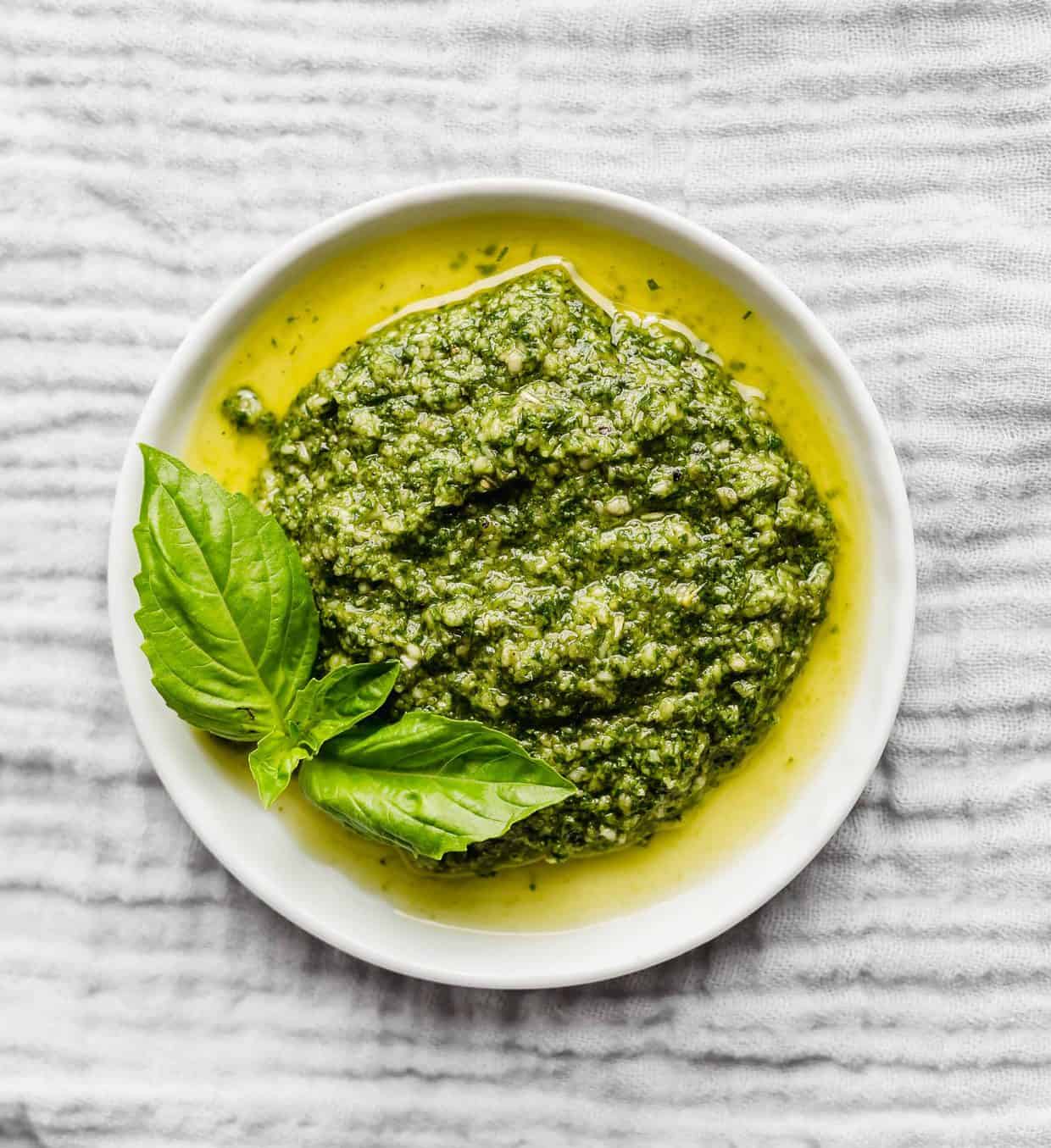 Green pesto on a white plate sitting on a grey napkin.