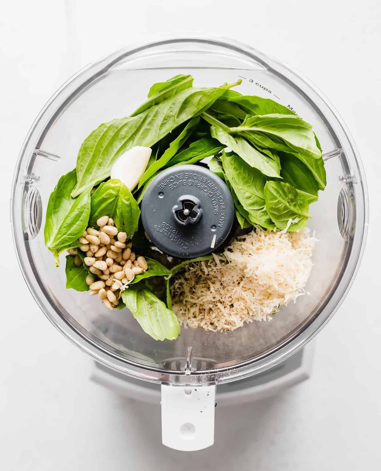 A food processor full of basil pesto ingredients.