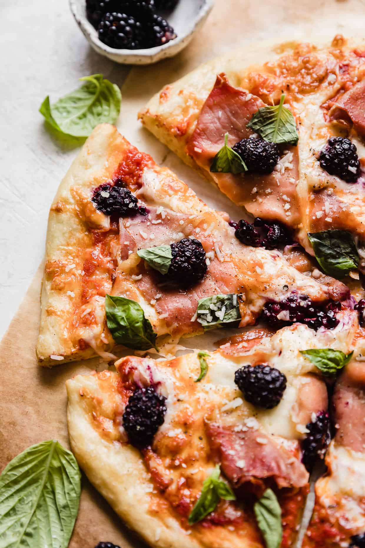 A slice of Blackberry Pizza topped with basil and proc prosciutto.