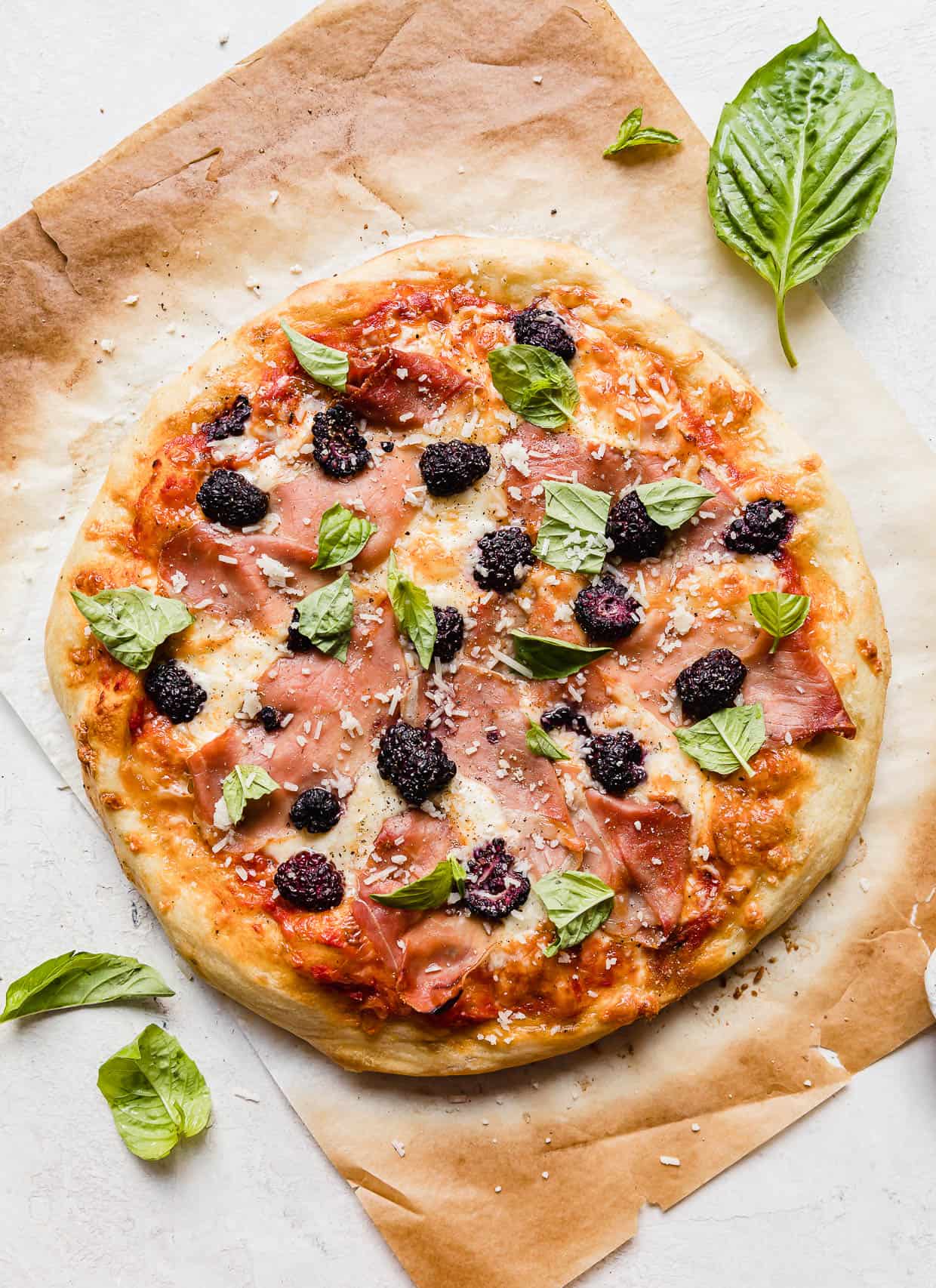 Blackberry pizza topped with fresh basil on a brown parchment paper.