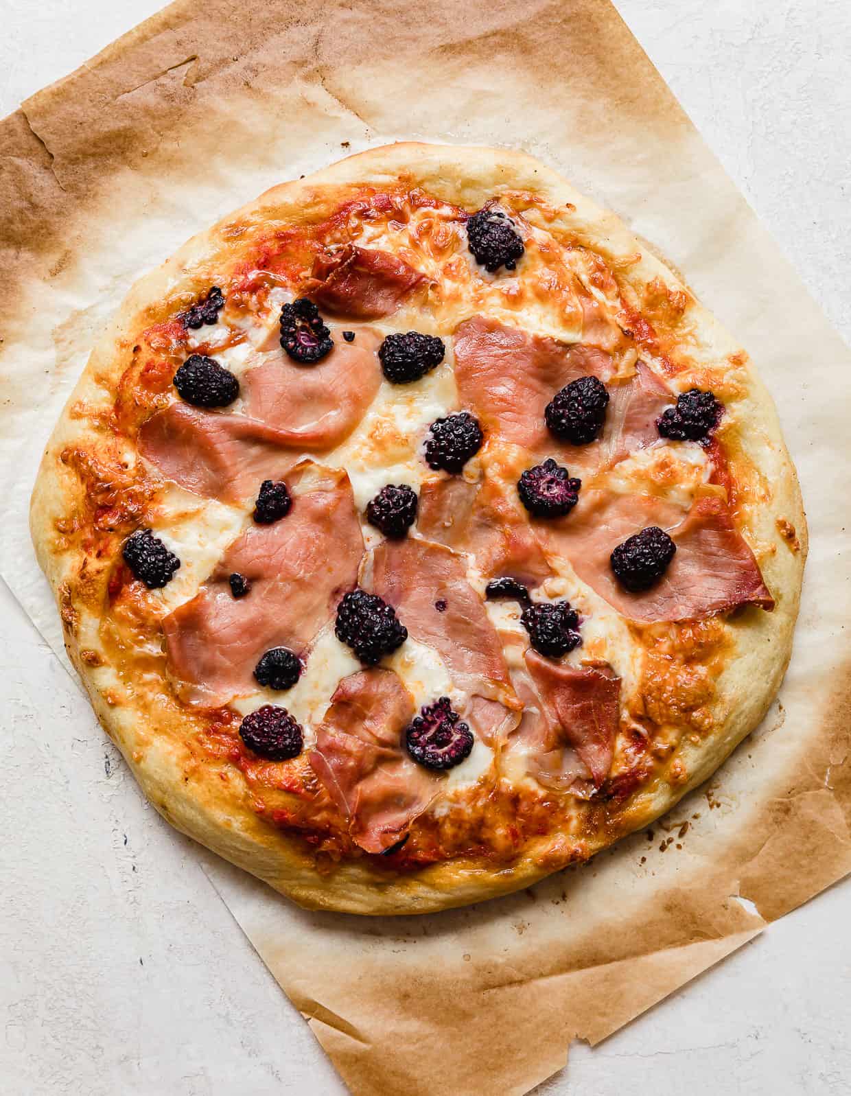 A baked blackberries pizza topped with prosciutto, basil, and blackberries.