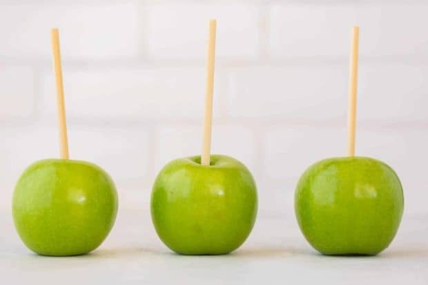 Three green apples with sticks poked into the stems.