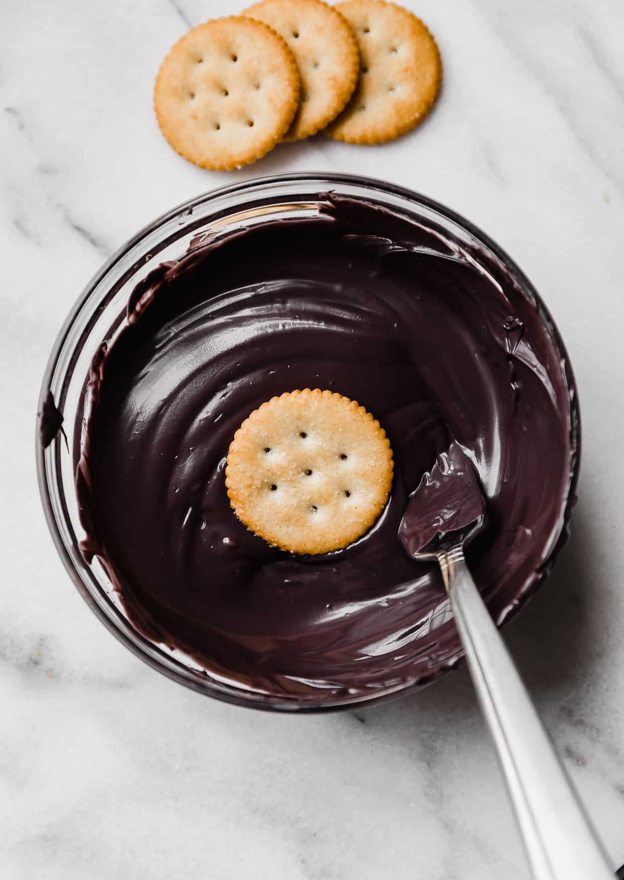 A ritz cracker in a bowl filled with black melted chocolate.