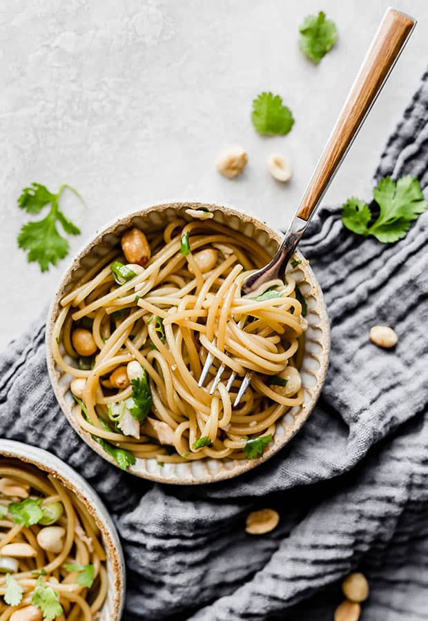 A bowl of sesame noodles and chopped cilantro, peanuts, and chicken.