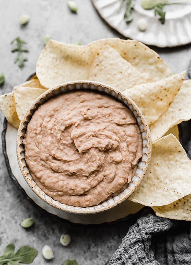 A bowl of slow cooker refried beans sitting on a plate surrounded by flour tortilla chips.