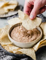 A hand dipping a flour tortilla chip into a bull full of slow cooker refried beans.