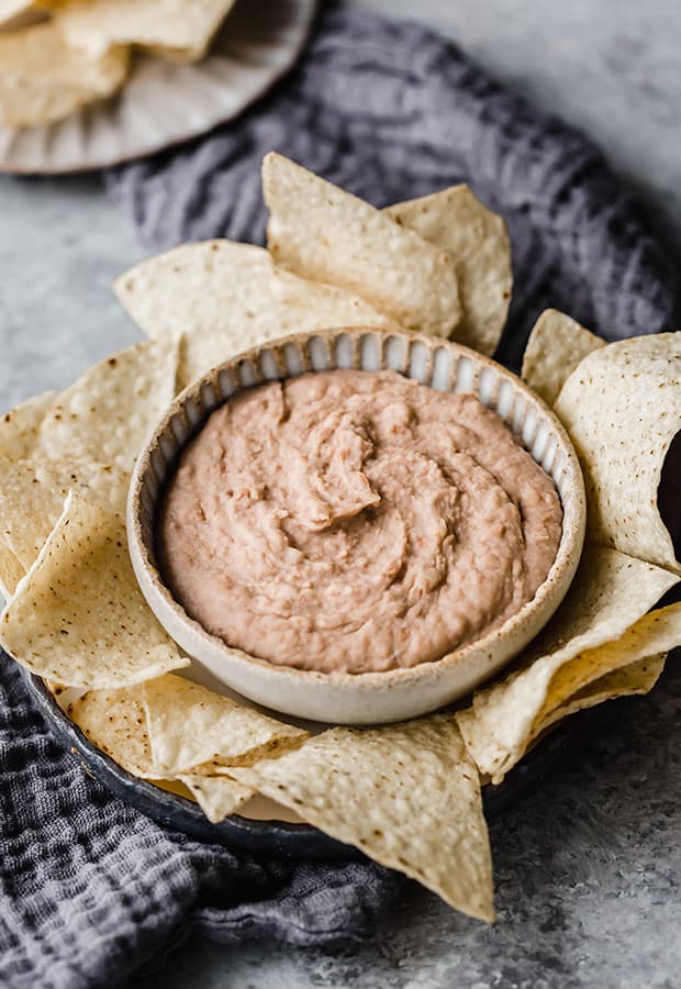 A bowl of refried beans with tortilla chips surrounding the perimeter of the bowl.