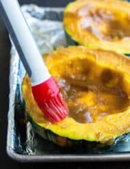 A red colored pastry brush is used to apply the buttery brown sugar mixture to the surface area of the winter squash.