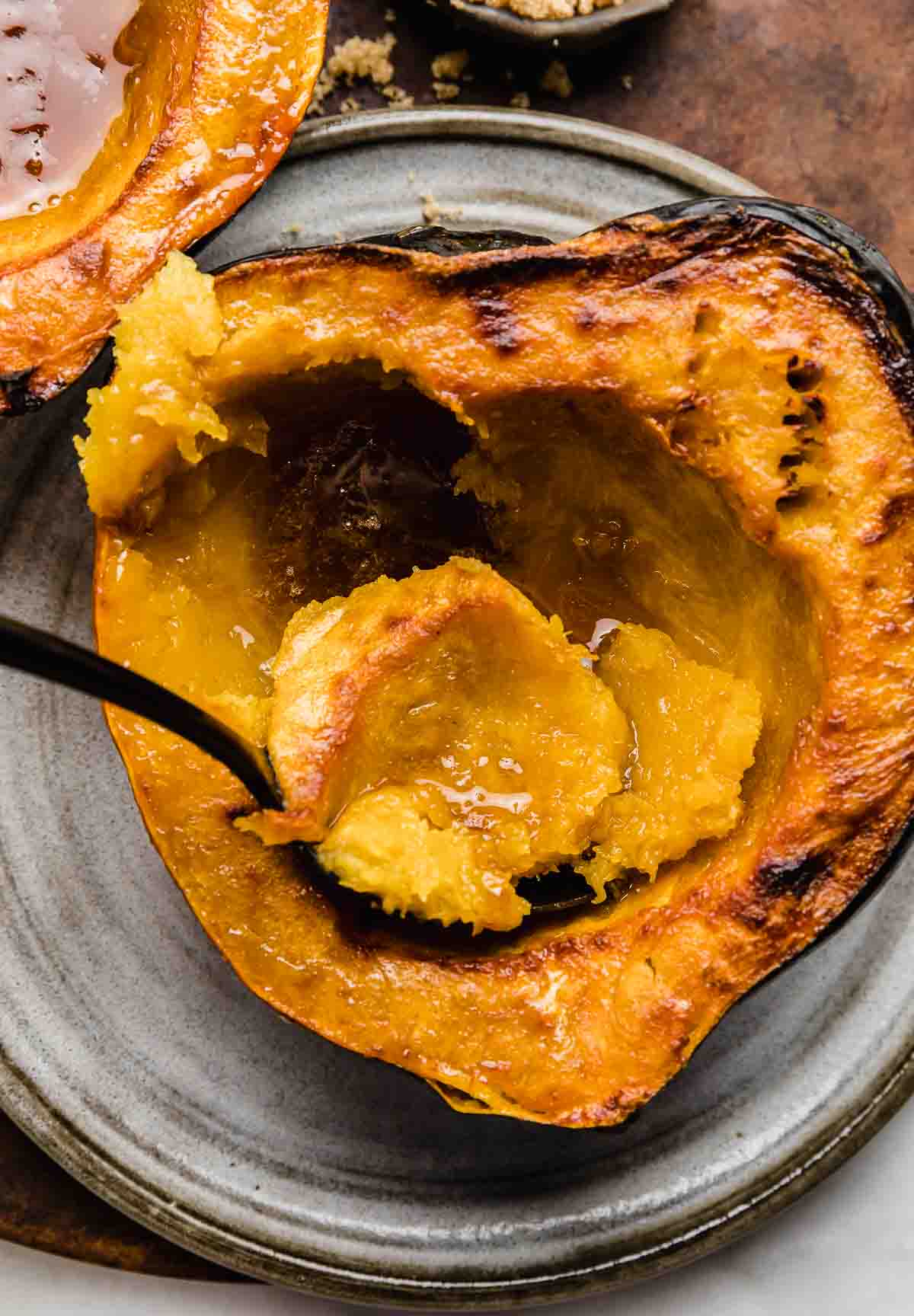 A spoon scooping out orange flesh from a bon bon winter squash with brown sugar.