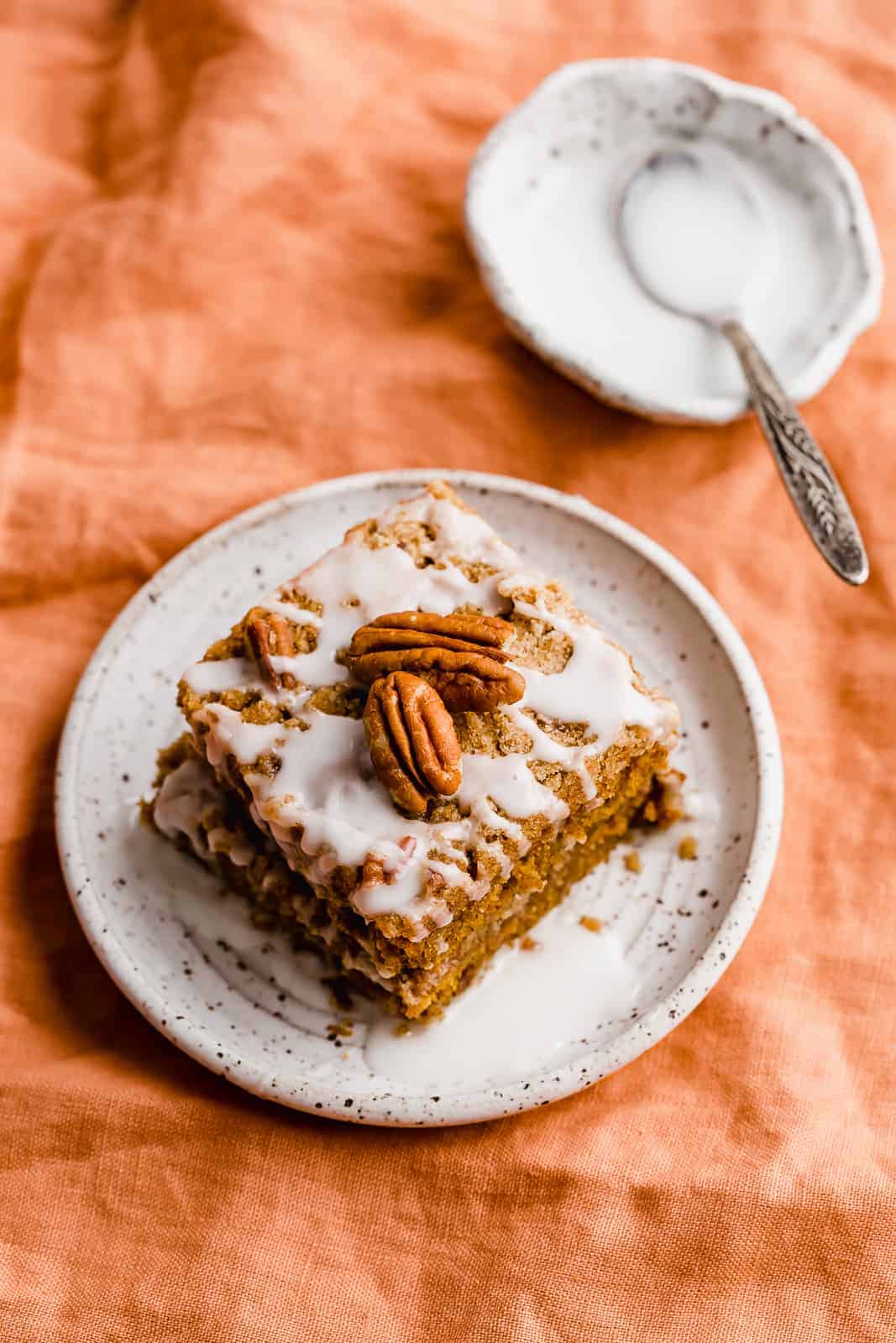 A slice of Pumpkin Coffee Cake on a white plate sitting on an orange linen napkin.