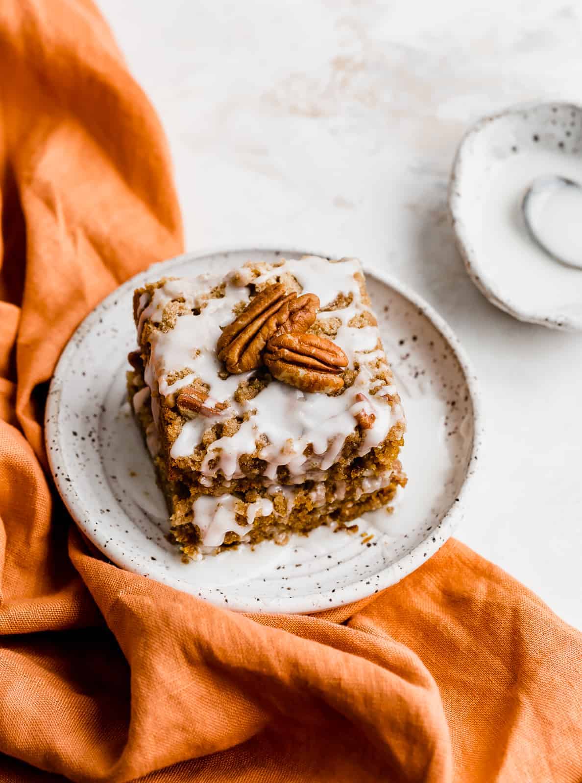 An orange napkin underneath a white plate with a slice of pumpkin coffee cake on top.