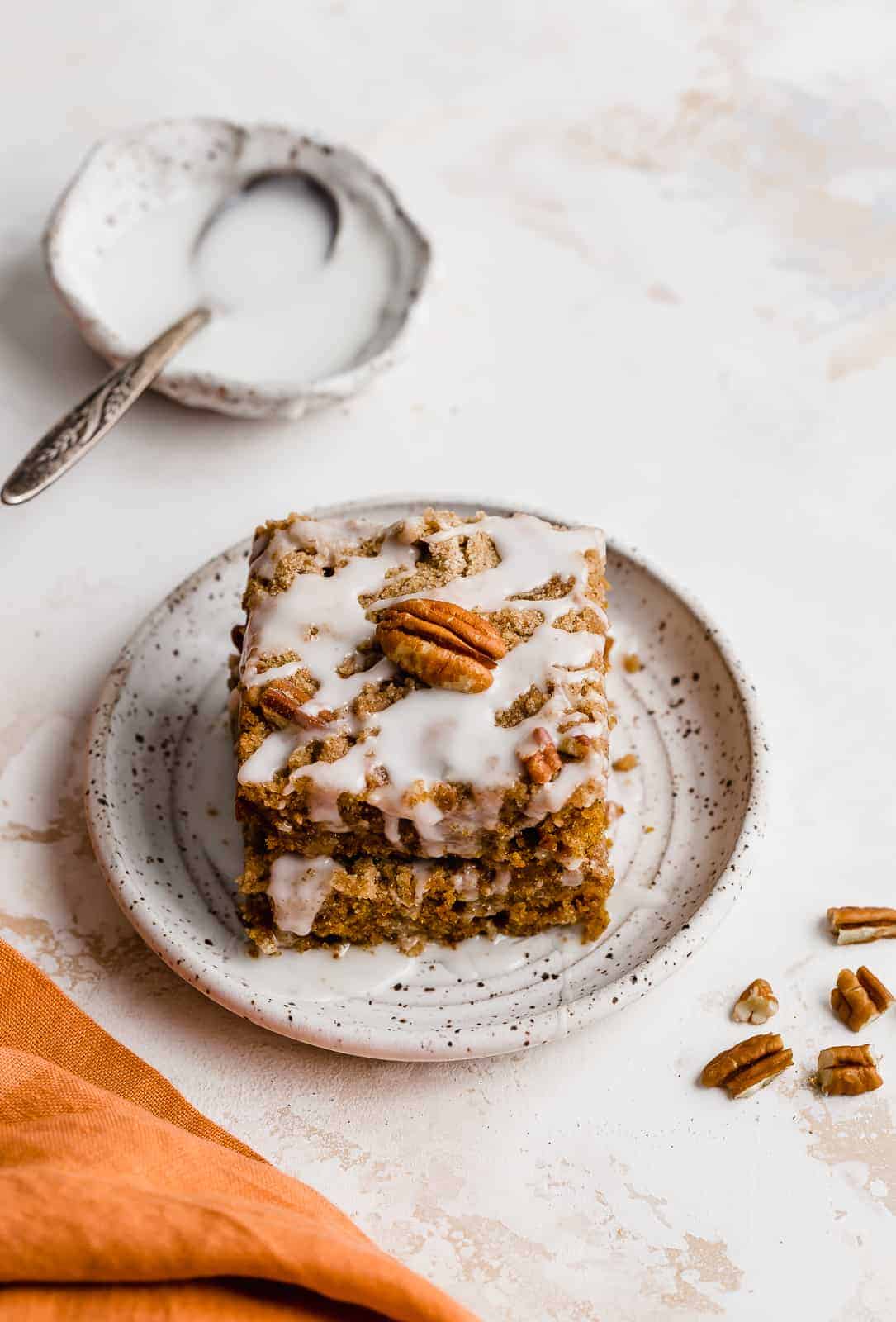 Pumpkin Coffee Cake with glaze, on white plate with chopped pecans next to the plate.