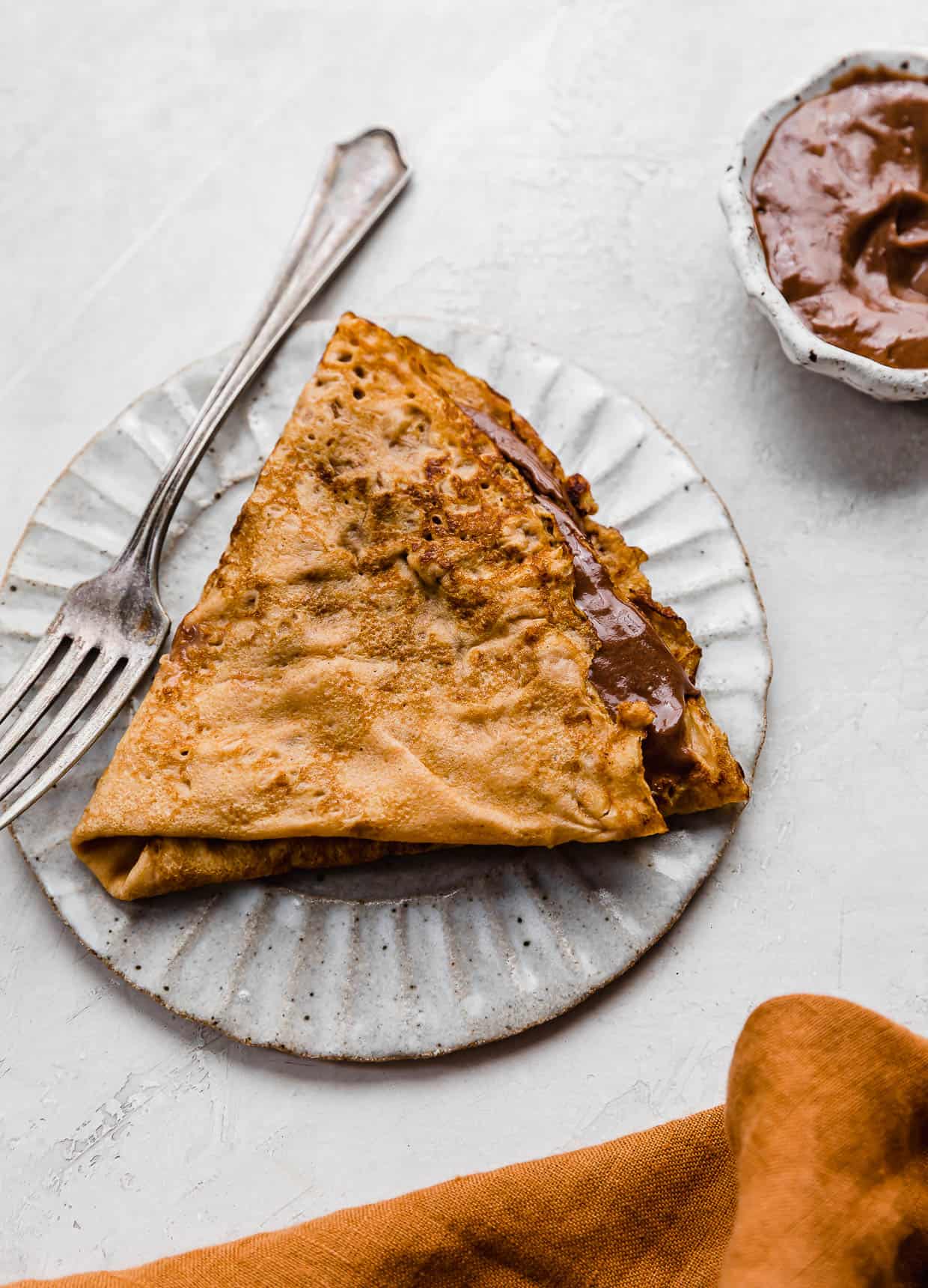 A Pumpkin Crepe filled with whipped nutella folded into a triangle, on a white plate.