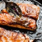 A spoon drizzling brown sugar and butter glaze overtop of a seared salmon filet.