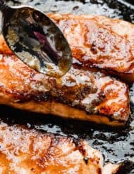A spoon drizzling brown sugar and butter glaze overtop of a seared salmon filet.