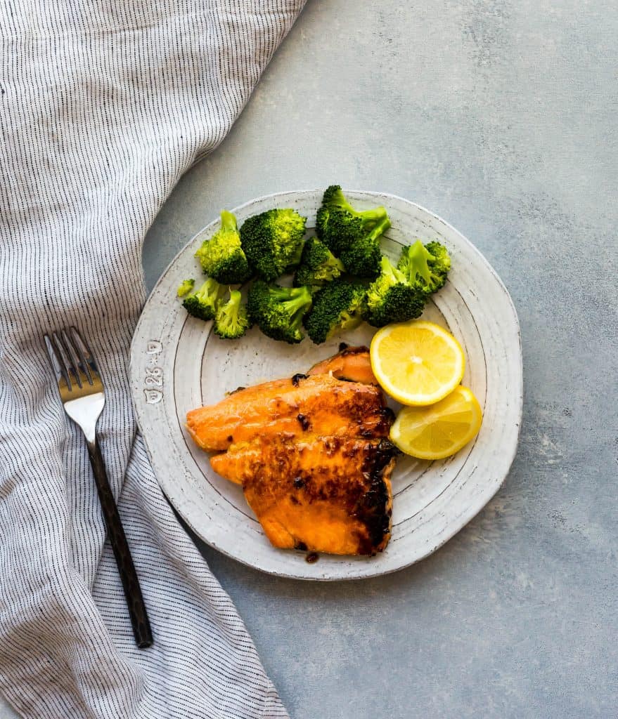 A salmon fillet, two lemon wedges, and a small pile of broccoli sitting on a white plate.