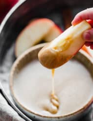 A hand dipping an apple into caramel dip.