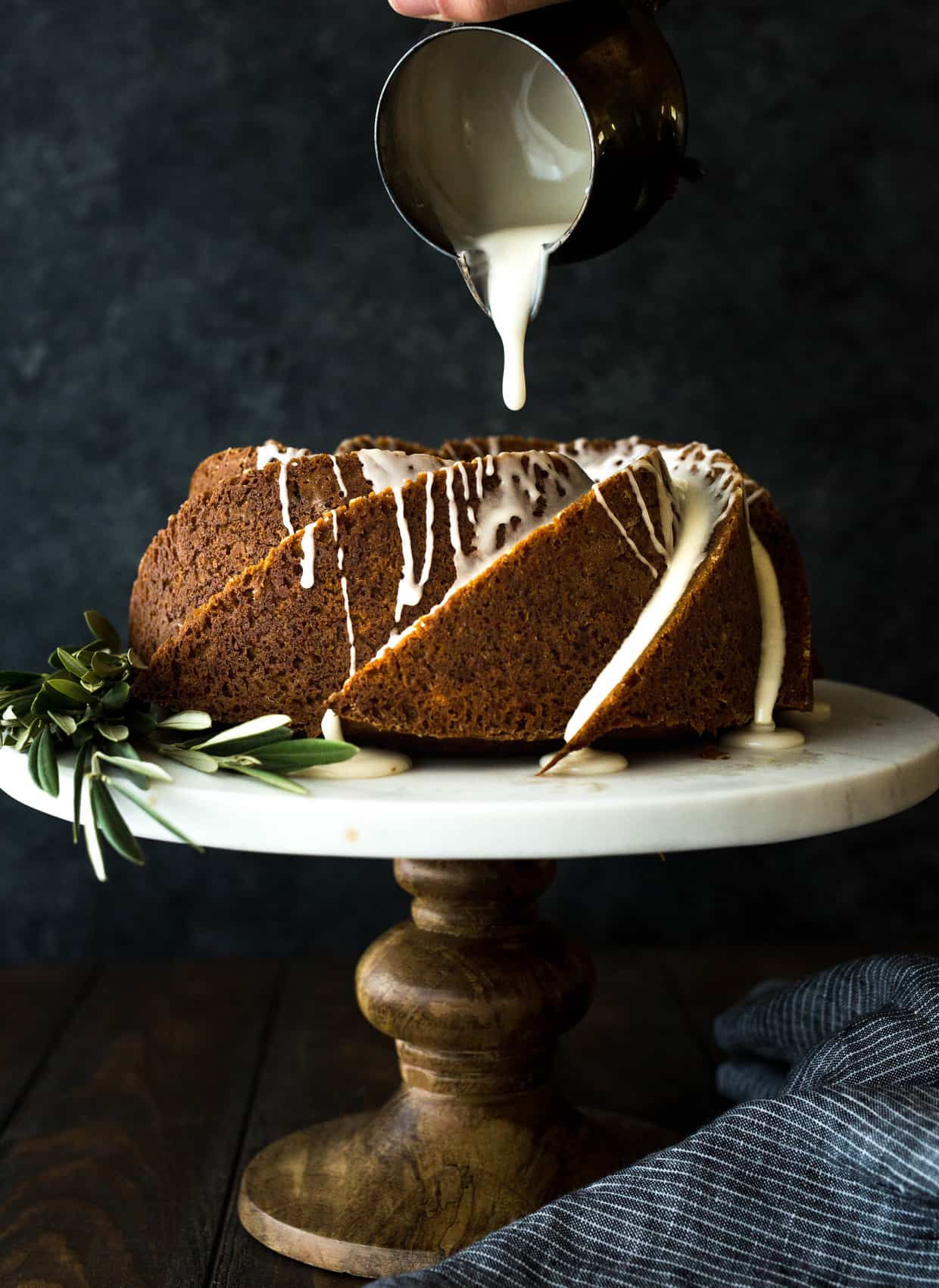 Gingerbread bundt cake sitting on a cake stand, with maple glaze slowly drizzling over the cake. 