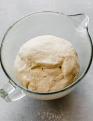 The best pizza dough recipe in a glass bowl, risen and ready to use.