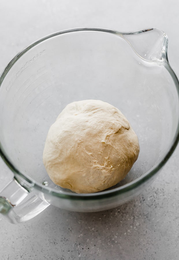 A glass bowl with homemade pizza dough in the bowl, prior to letting the dough rise.