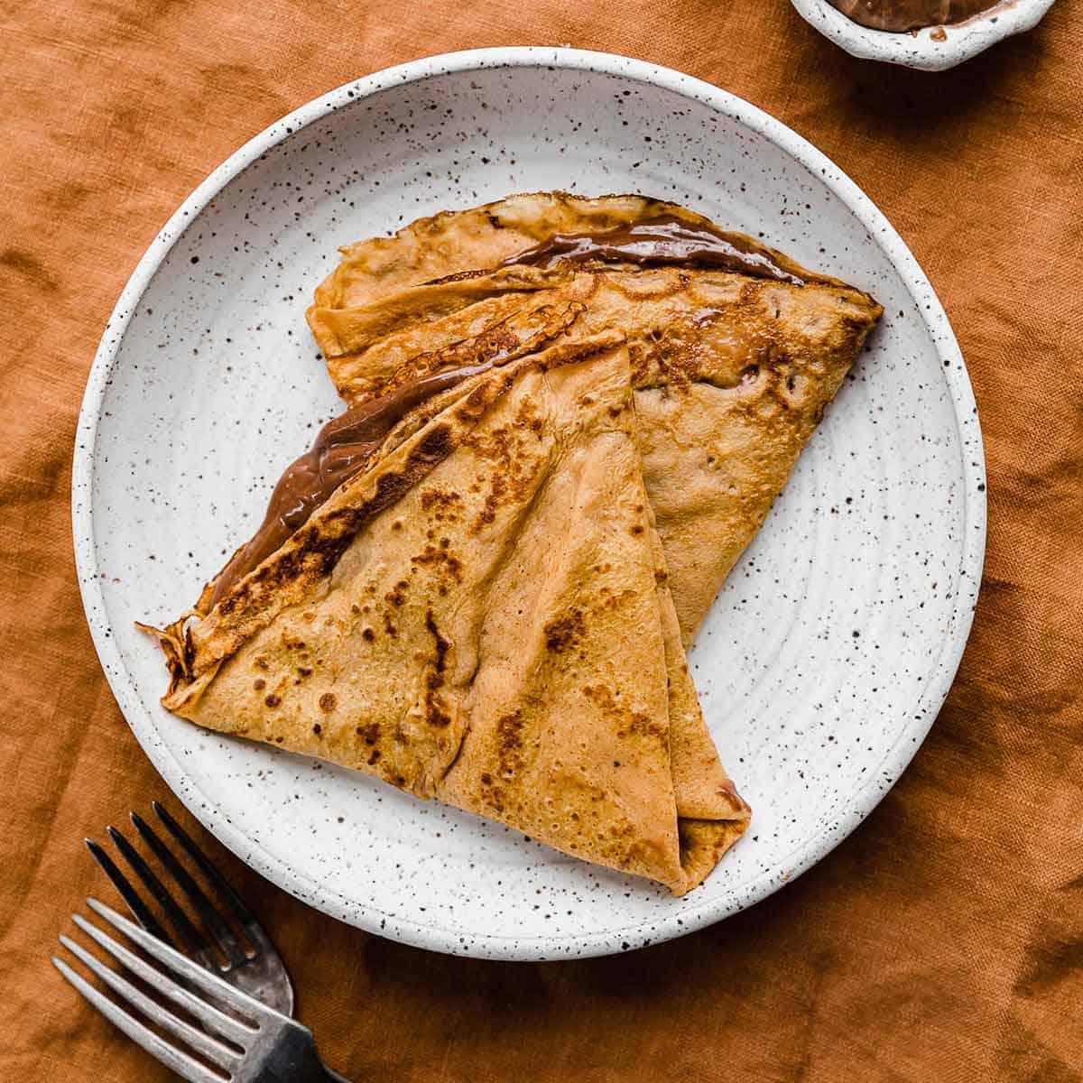 Two Nutella filled pumpkin crepes on a white plate.