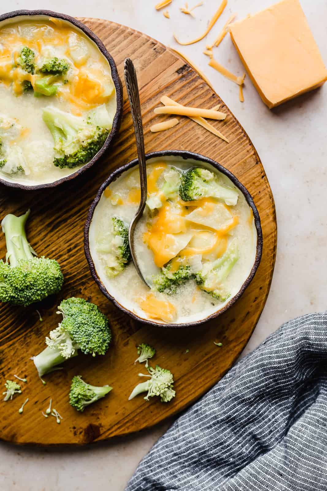 Two bowls of broccoli potato soup on a brown circular board.