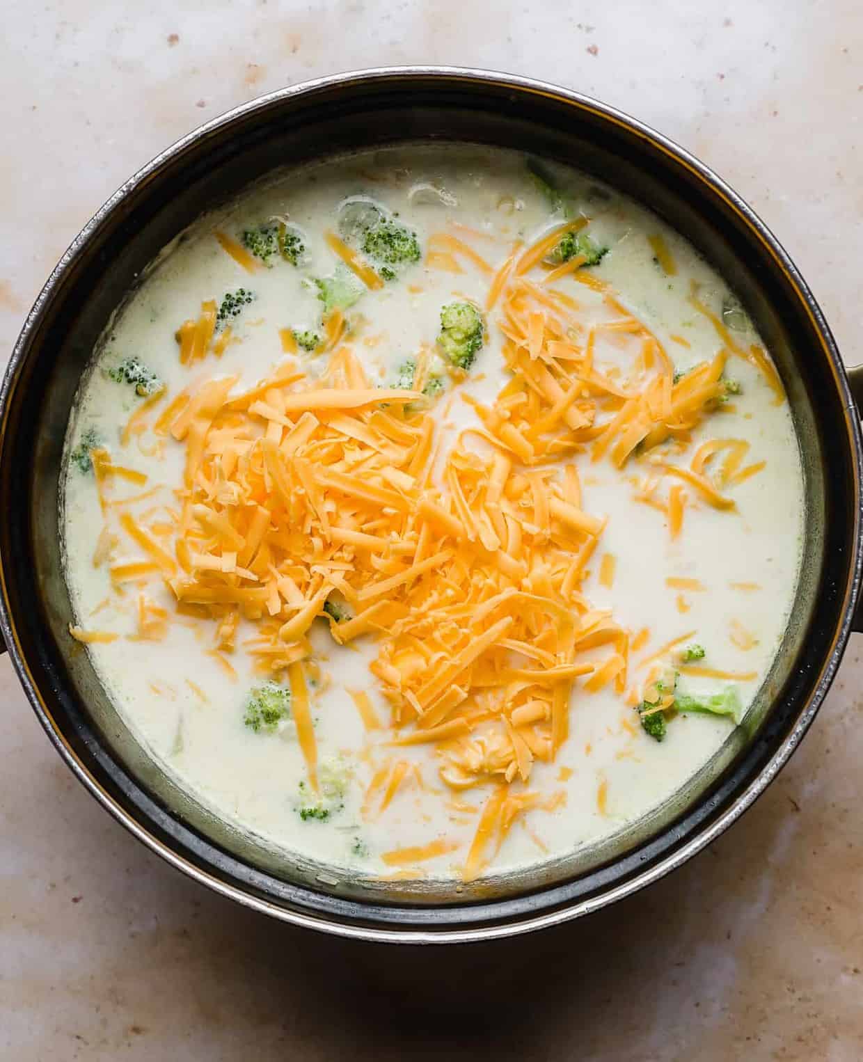 a large pot with shredded cheddar cheese spread over the top of broccoli potato soup.