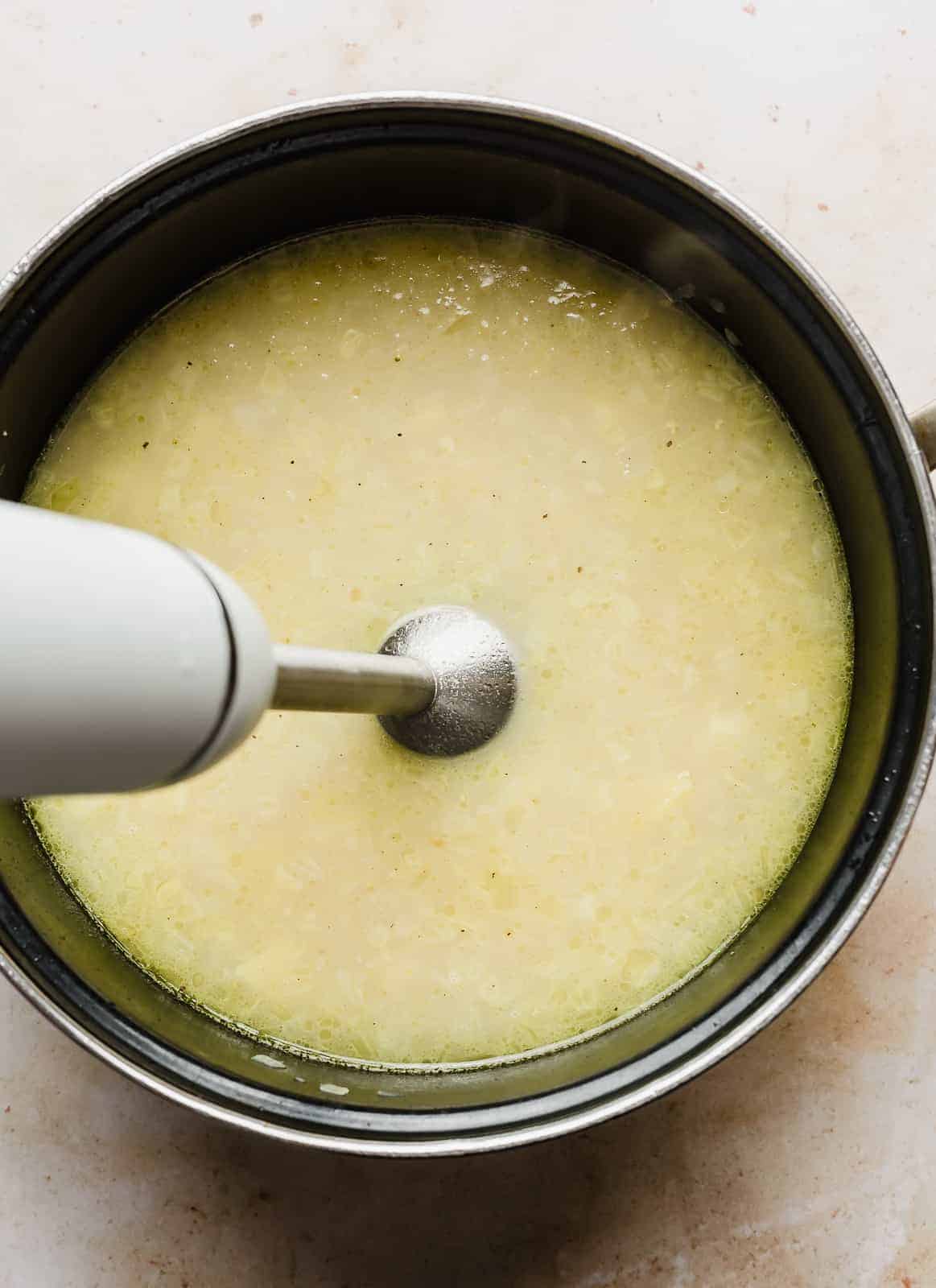 An immersion blender mixing soup in a large pot.