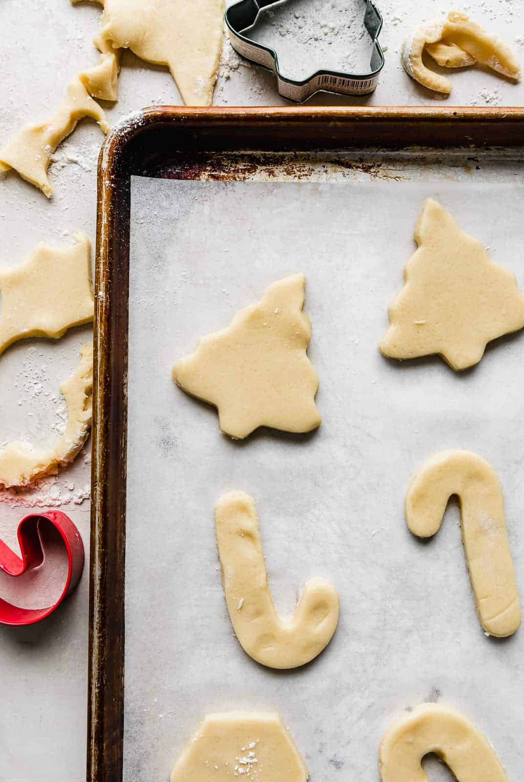 Sugar cookie dough cut into a tree and candy canes on a parchment lined baking sheet.