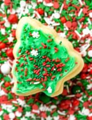 A never fail Christmas tree shaped sugar cookie on top a plate of sprinkles.