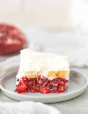 A square slice of Christmas pomegranate Jell-O, topped with bananas and whipped cream.
