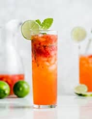 A tall mojito glass filled with a strawberry mojito mocktail with a lime wedge on the rim.