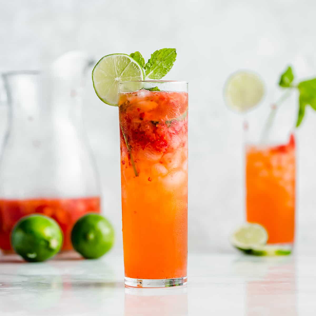 A tall mojito glass filled with a strawberry mojito mocktail with a lime wedge on the rim.