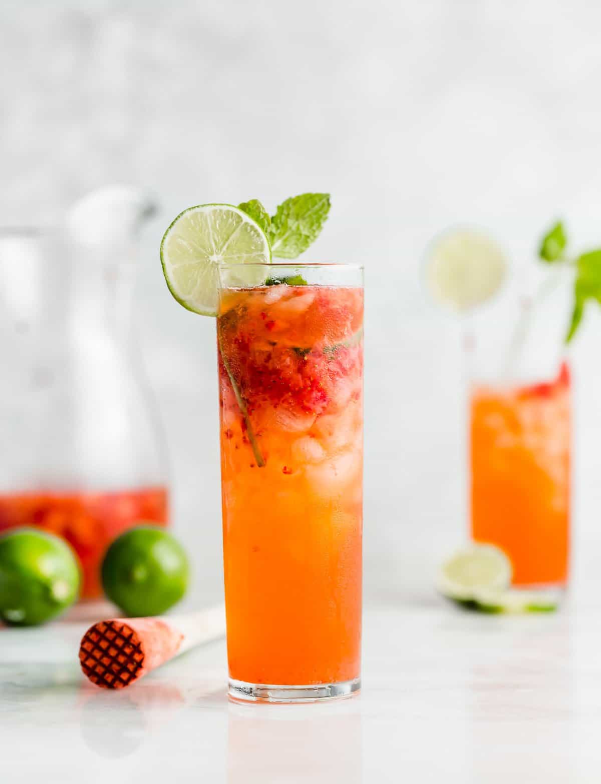 A tall mojito glass filled with a Strawberry Mocktail and ice with a lime wedge on the rim.