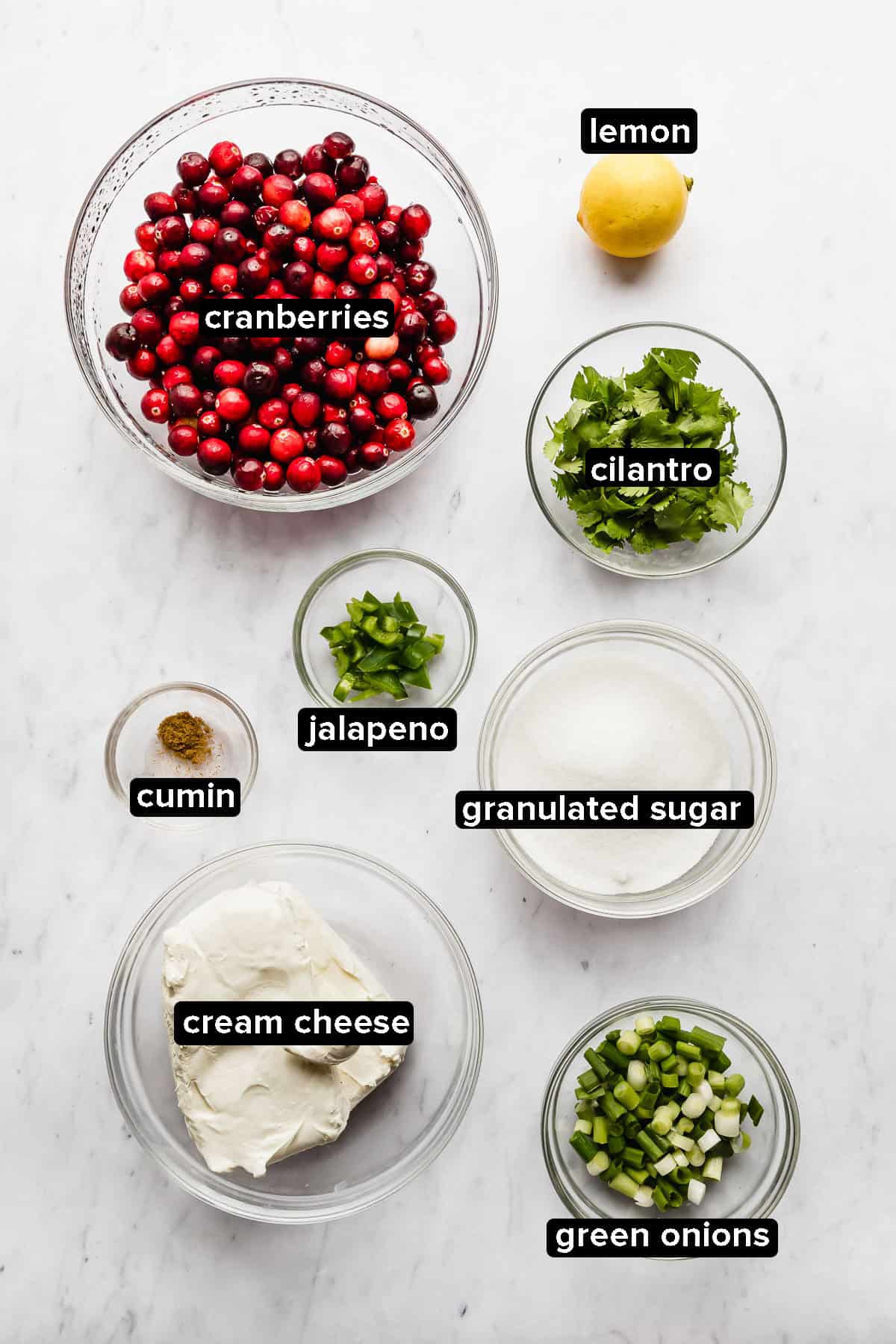 Cranberry cilantro dip ingredients in glass bowls on a white background.
