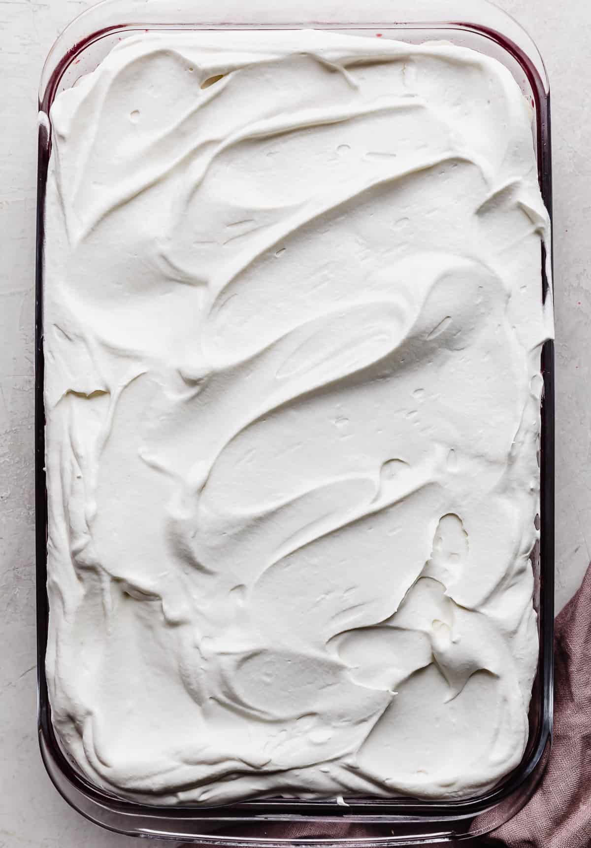 Whipped cream covering a Pomegranate Jell-O in a glass rectangular baking dish.