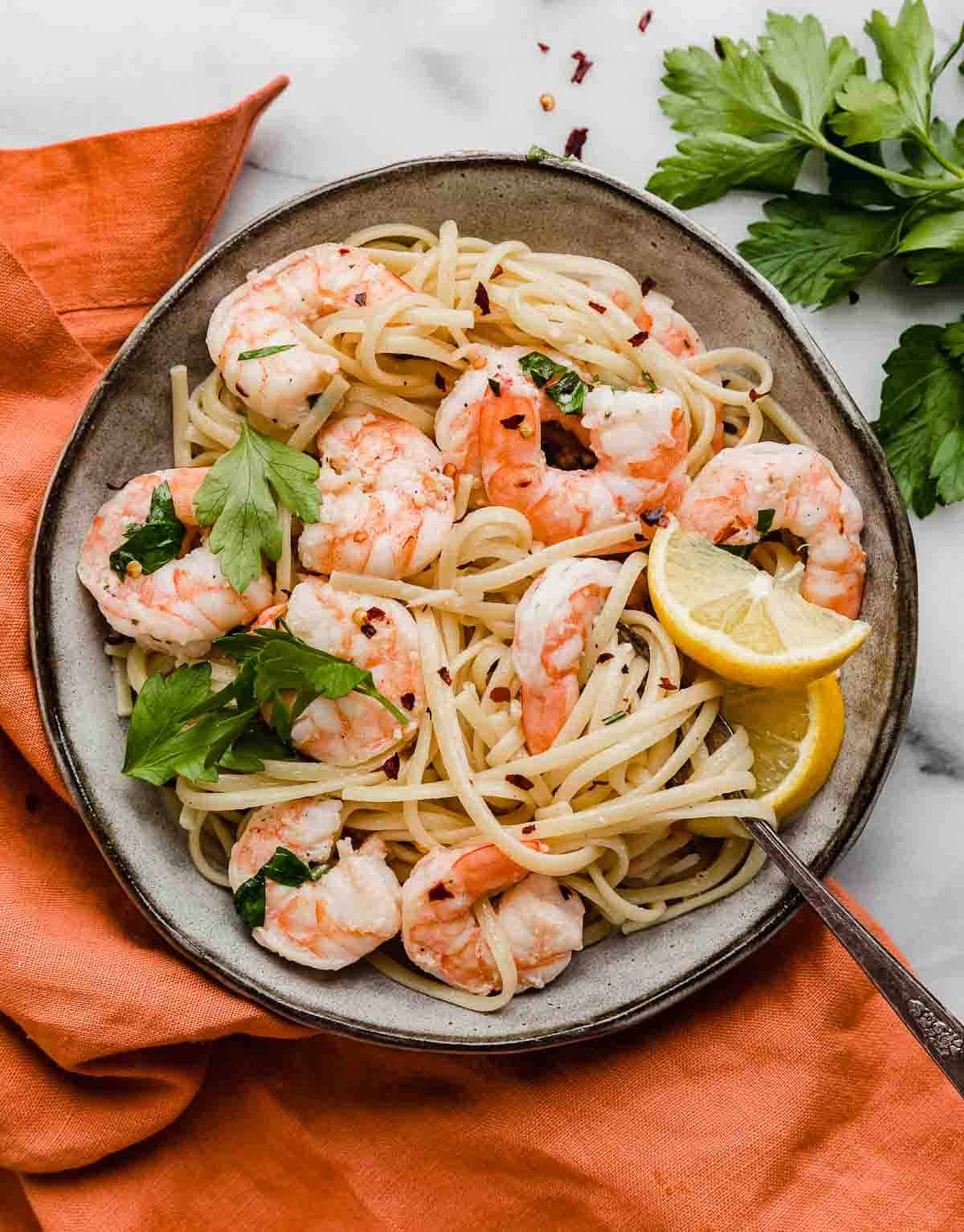 A gray pasta bowl filled with linguine noodles topped with red pepper flakes and cooked pink shrimp.