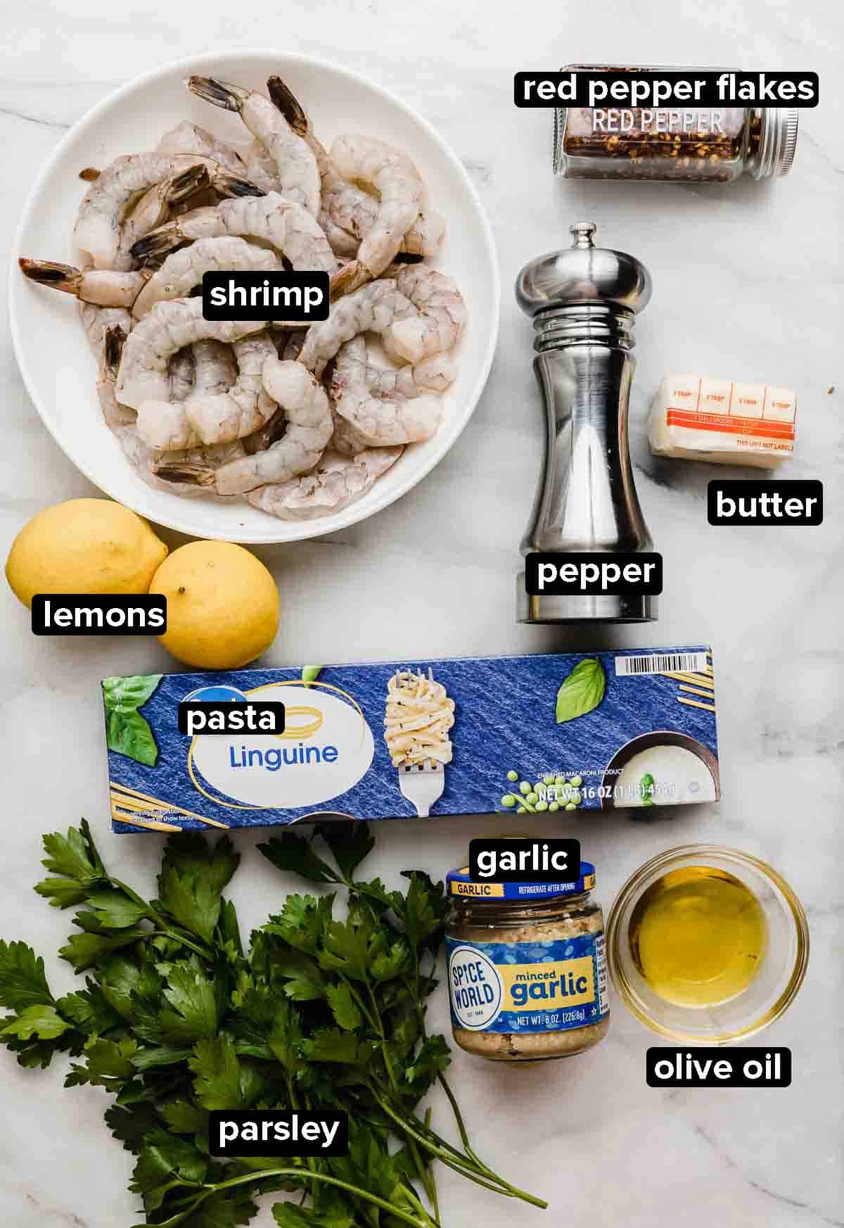 Shrimp Scampi with Linguine ingredients on a white background: parsley, shrimp, lemons, garlic, linguine noodles, butter, and pepper.