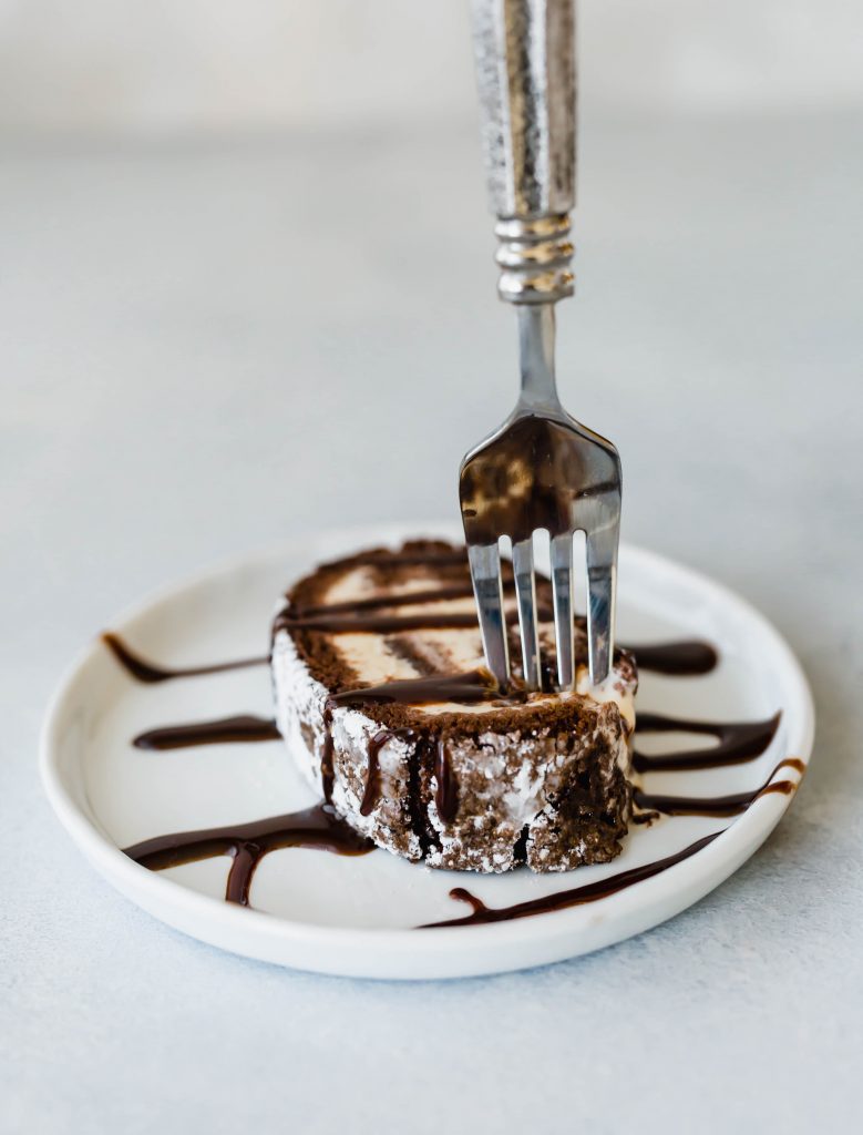 Ice cream cake roll covered in hot fudge, and a fork digging into the cake. 