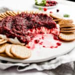 A white plate with a cranberry cream cheese dip surrounded by round crackers.