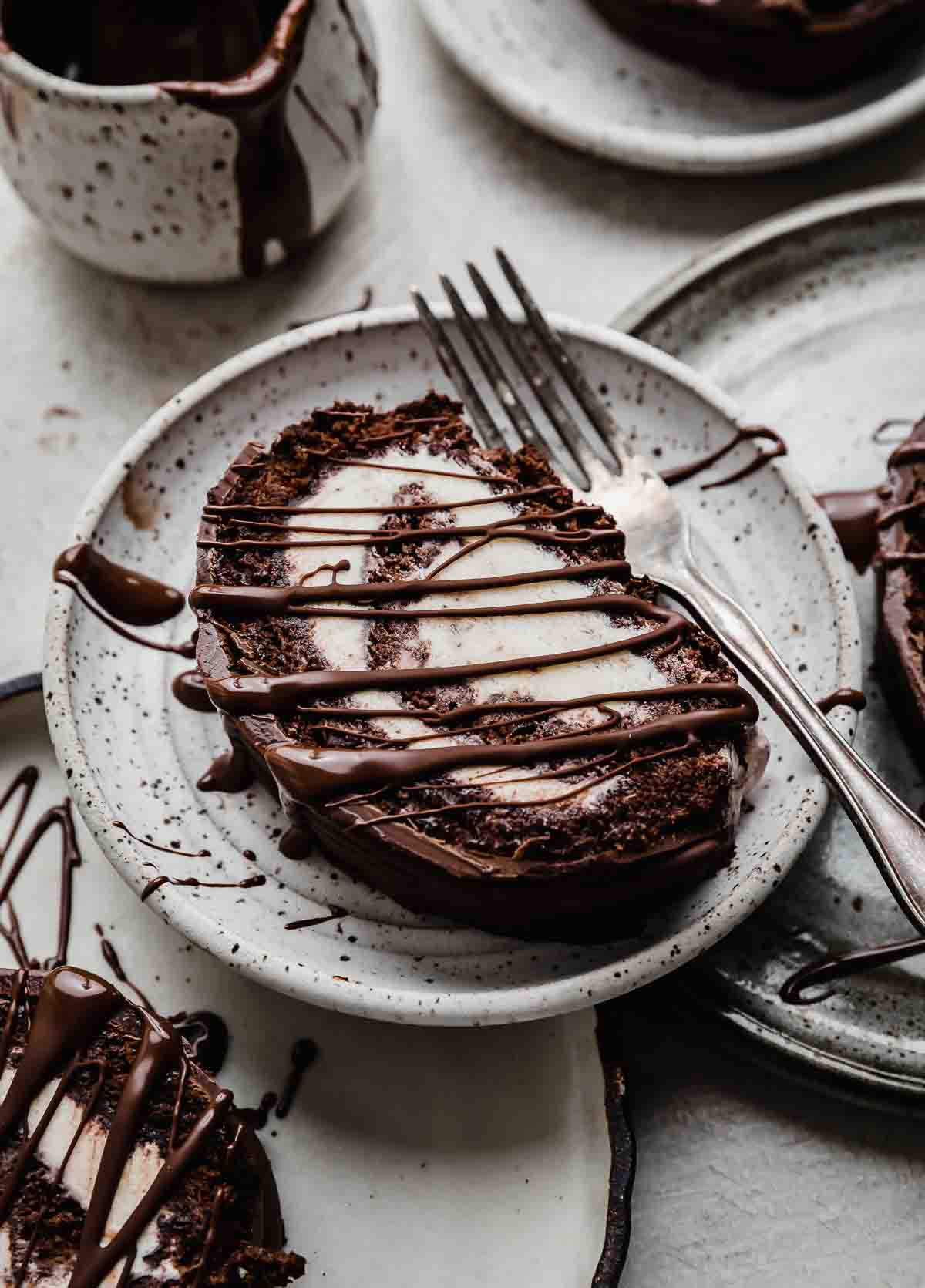 Chocolate cake roll rolled up with vanilla ice cream and drizzled with magic shell on a white plate.