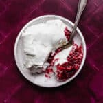 A slice of whipped topping covered Christmas Pomegranate Jell-O on a plum colored background.