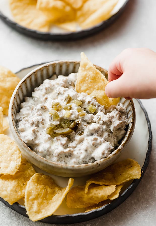 A hand dipping a chip into sausage dip.
