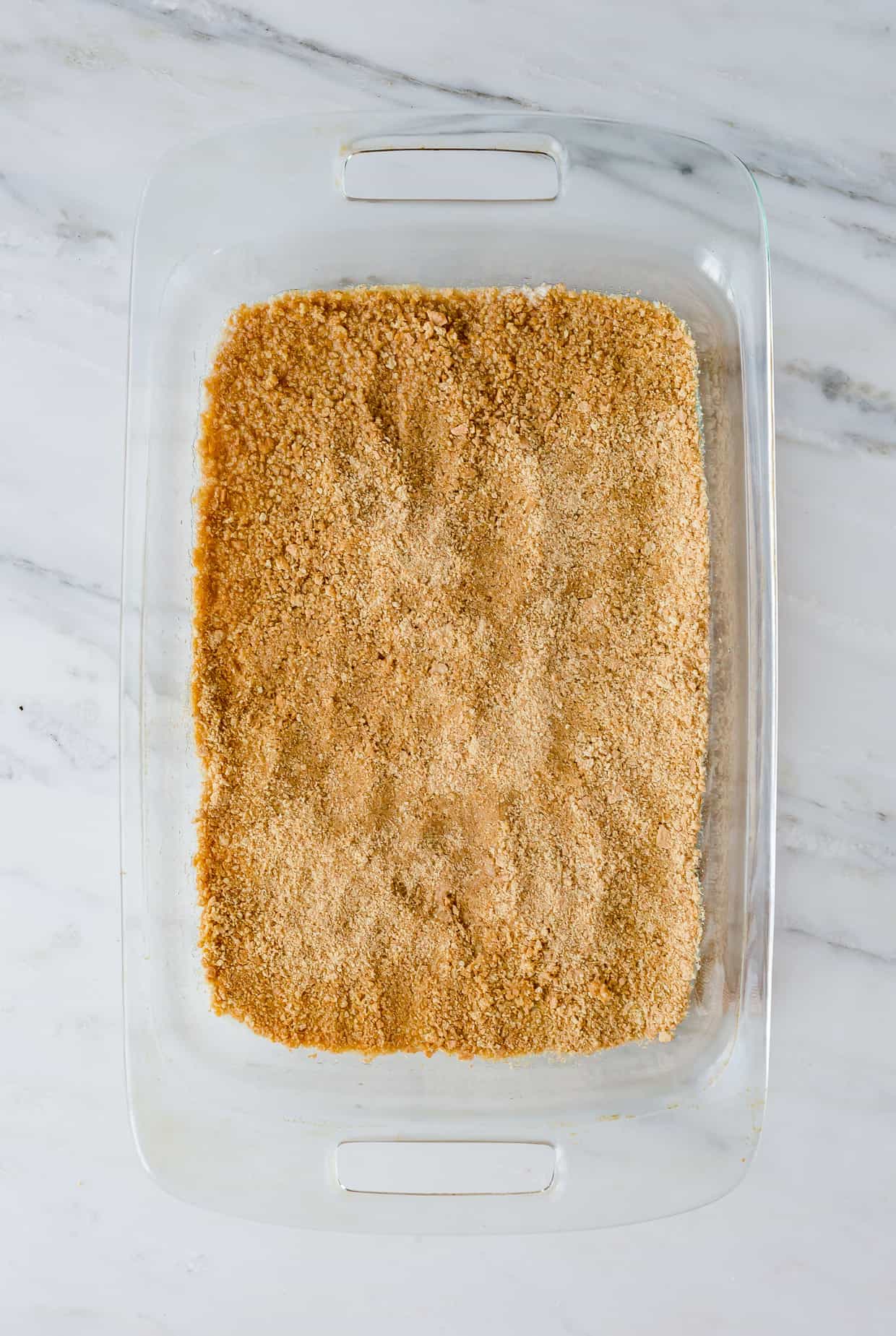 A graham cracker crust filling the bottom of a 9 x 13 inch pan for 7 Layer Bars.